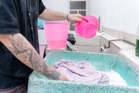 A young Hispanic woman is handwashing a pink sweatshirt on a traditional sink. Concept of laundry tasks at home