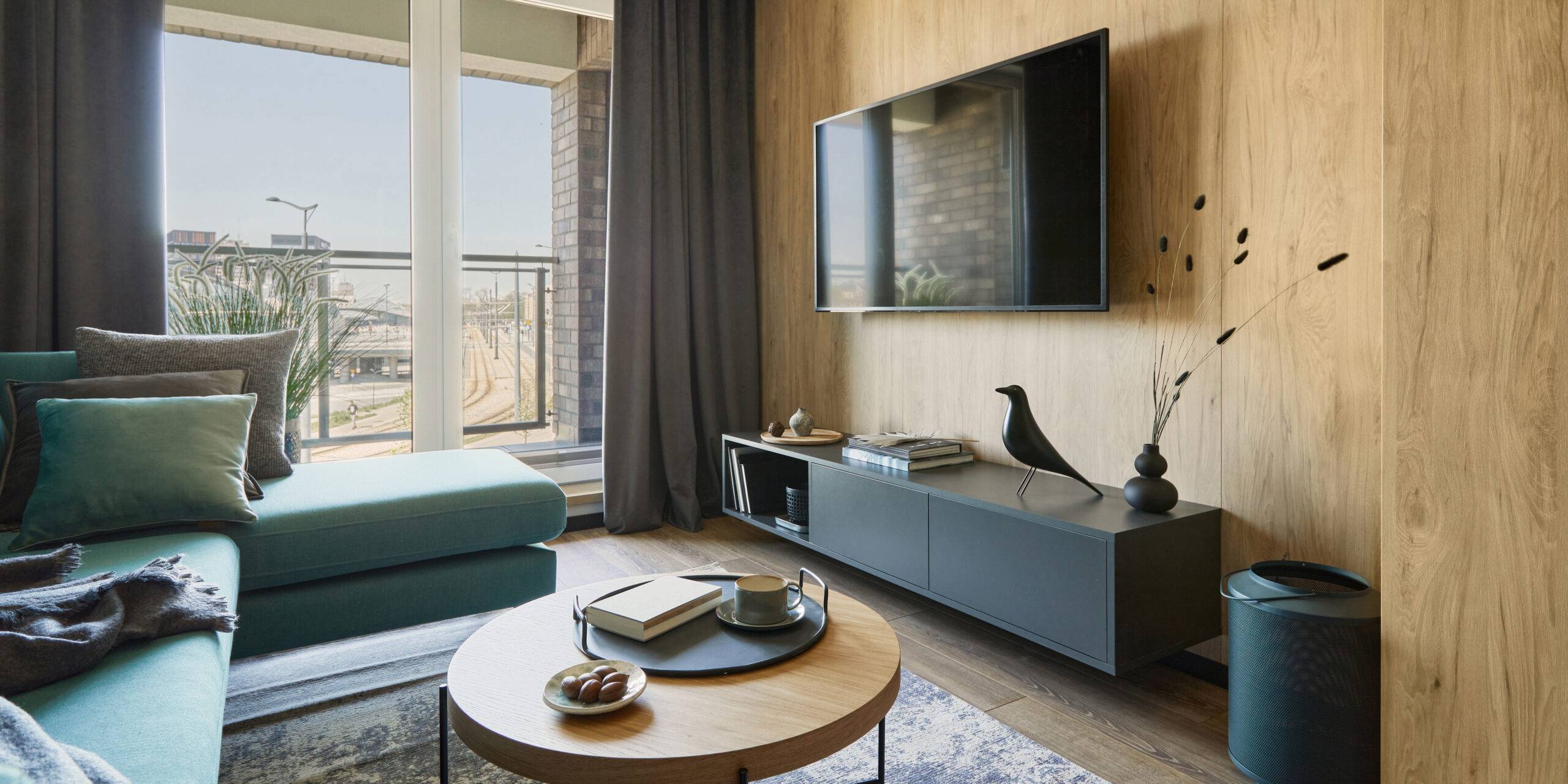 Creative composition of modern living room interior in small apartment. Eucalyptus sofa, designed coffee table, black commode and personal accessories. Big windows with a big city view on. Template.