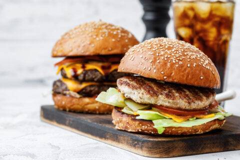 Freshly cooked burger on wooden board on light background, front view