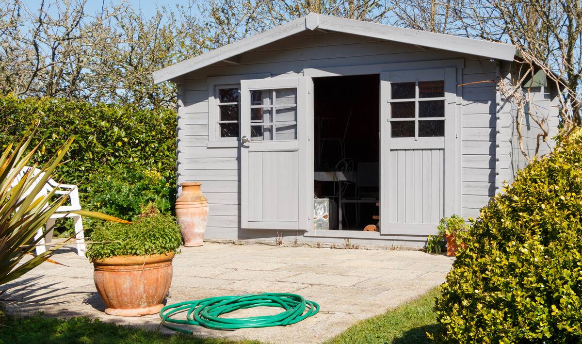 A grey plastic shed in a backyard, a stone landing in front of it.