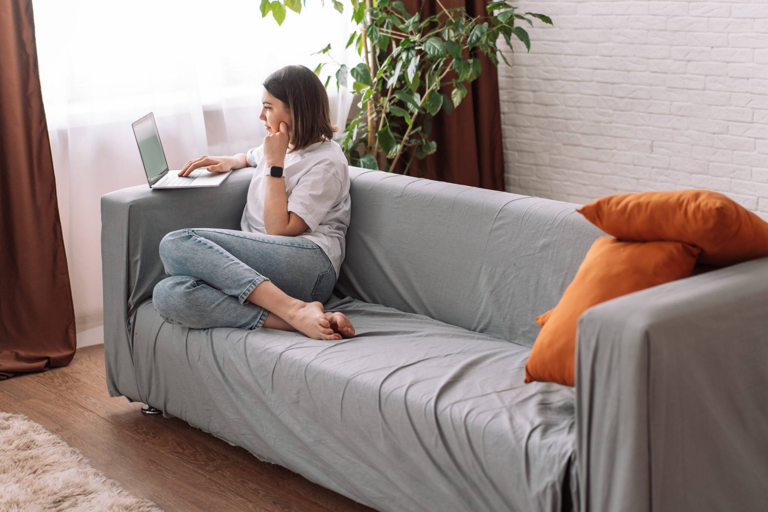 Lady teacher sitting on a gray sofa working with a laptop.