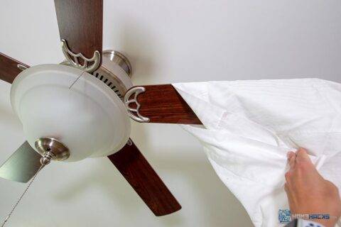 A person putting a pillowcase over the blade of a ceiling fan.