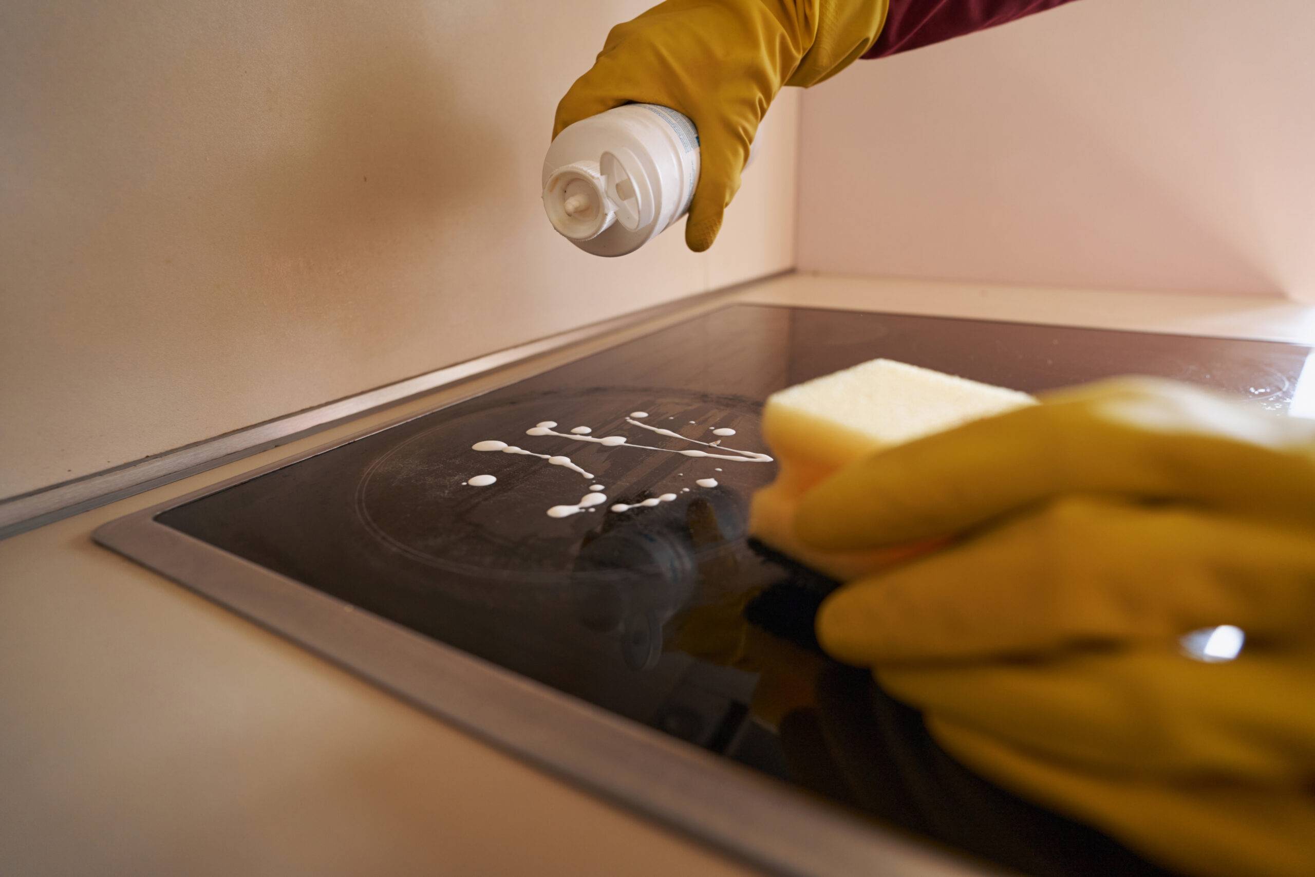 Cropped photo of hands in rubber gloves pouring cleaning agent on cooking surface