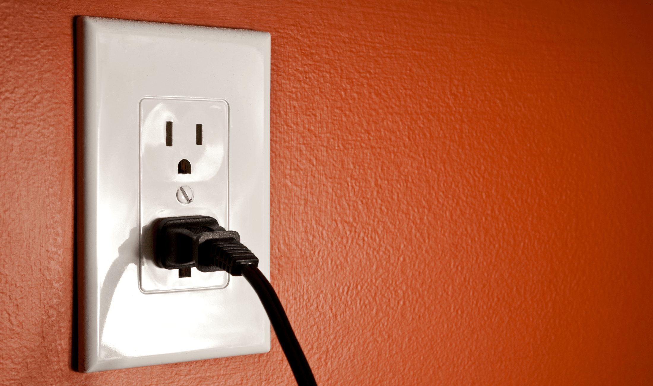 An electrical outlet on an orange wall, one cable plugged in.