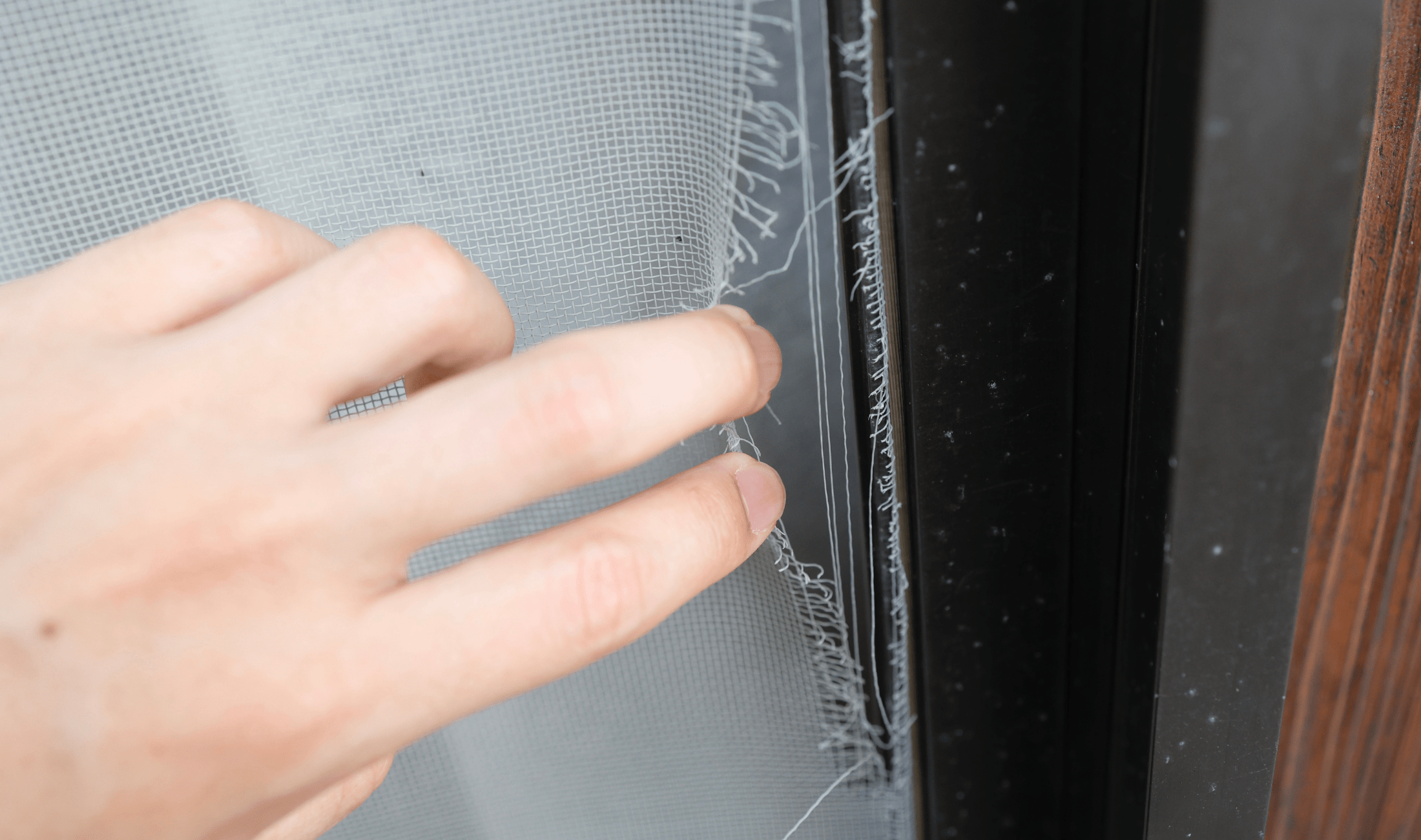 A hand pulling at a hole in a screen.