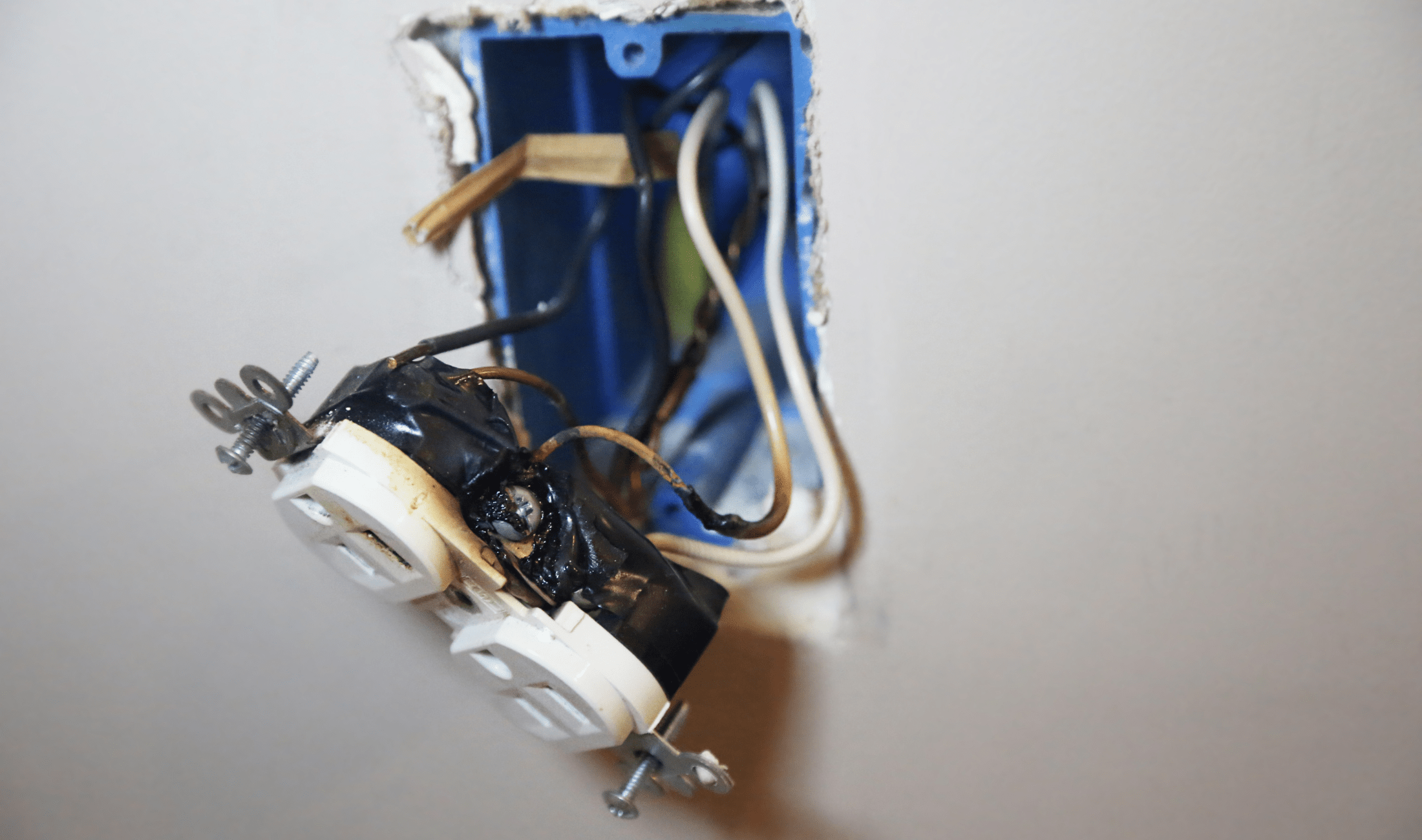An outlet hganging out of the wall, having clearly sparked or caught fire.