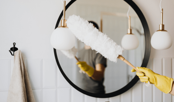 A person using a long feather duster on a light fixture.