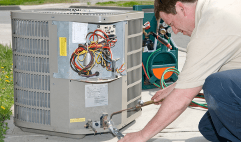 A man knelt over fixing an outdoor AC unit.